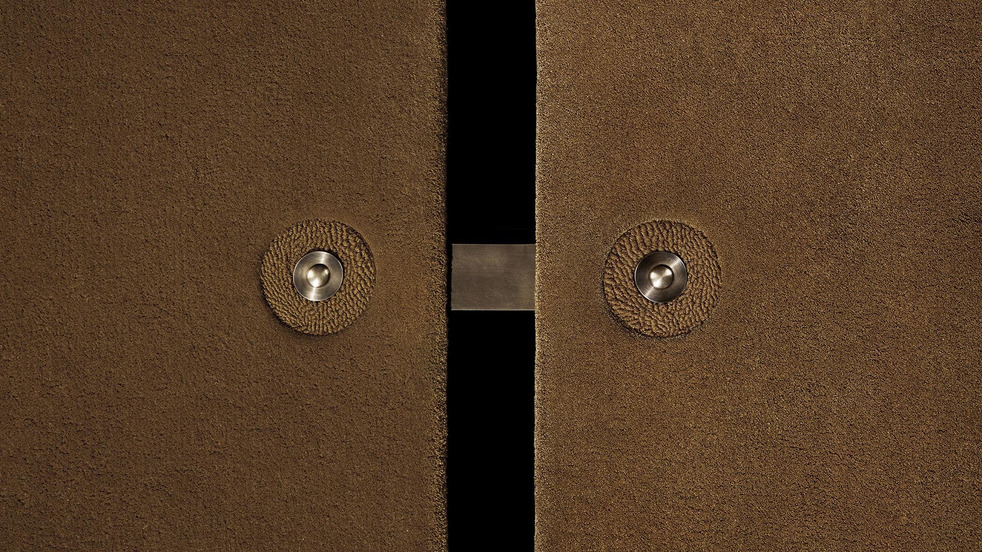Close-up of two brown textured panels with round metallic fasteners and a gap showing black space between them