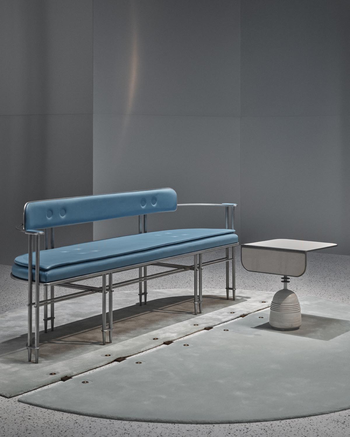 Minimalist room with a blue cushioned bench with chrome legs beside a small modern side table on a gray floor