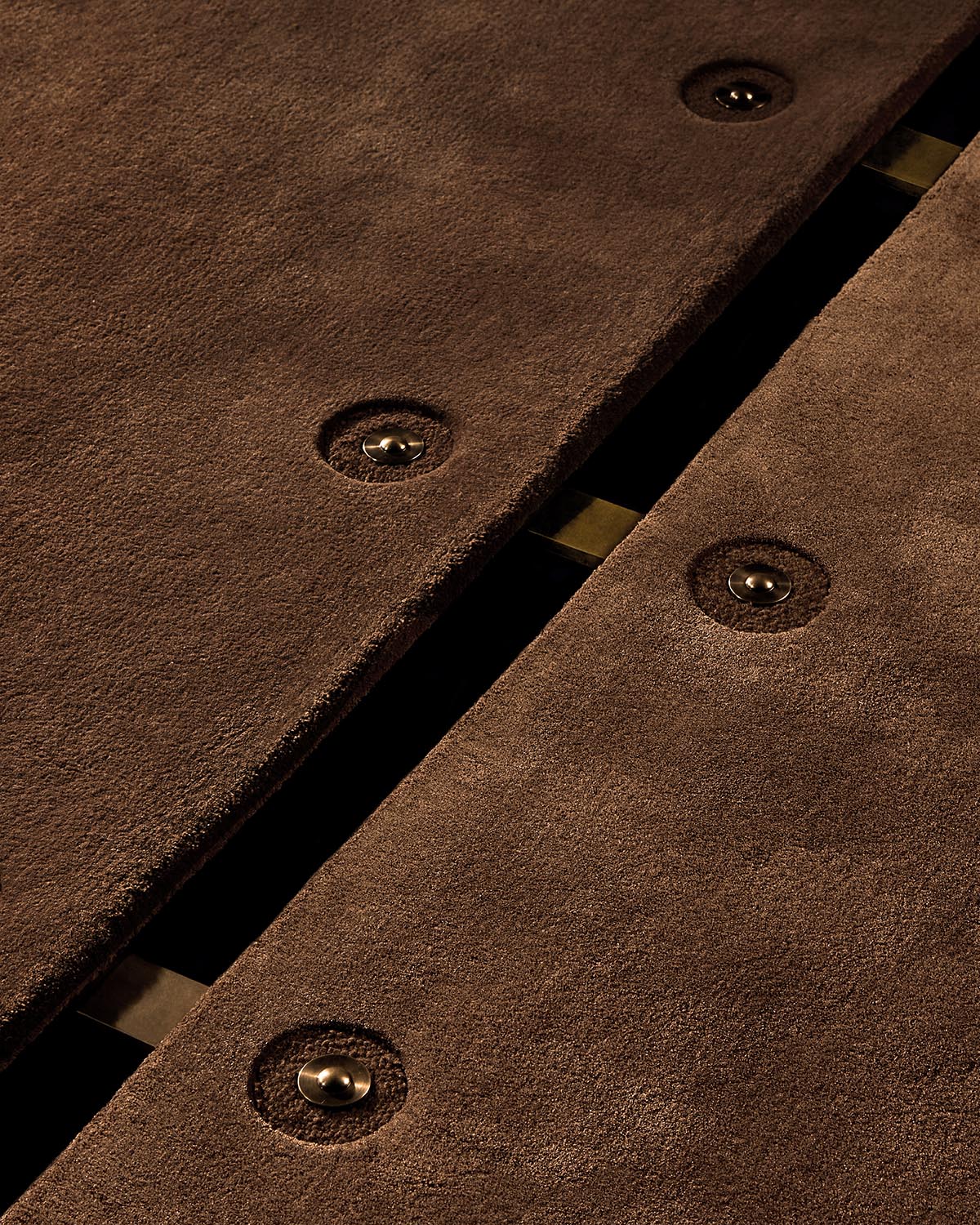 Close-up of overlapping brown suede material with circular metal snap buttons and a black background gap between panels