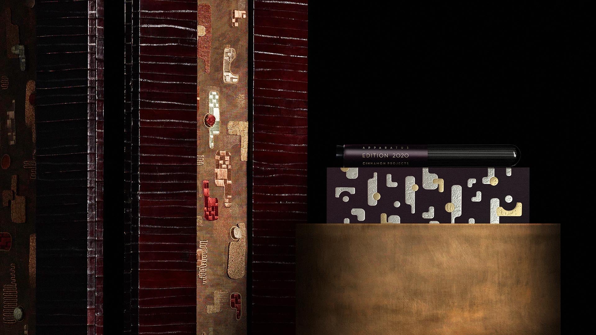 Close-up of stacked books with abstract patterned covers on a cylindrical bronze pedestal against a black background