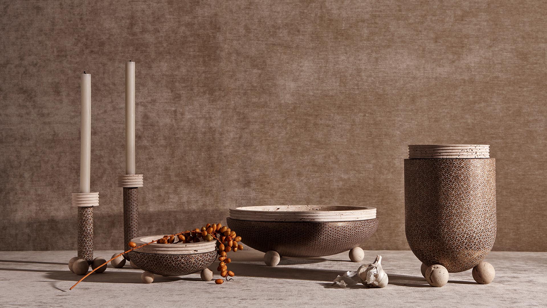 Collection of textured ceramic vessels and candle holders with natural decor arranged on a neutral surface and background
