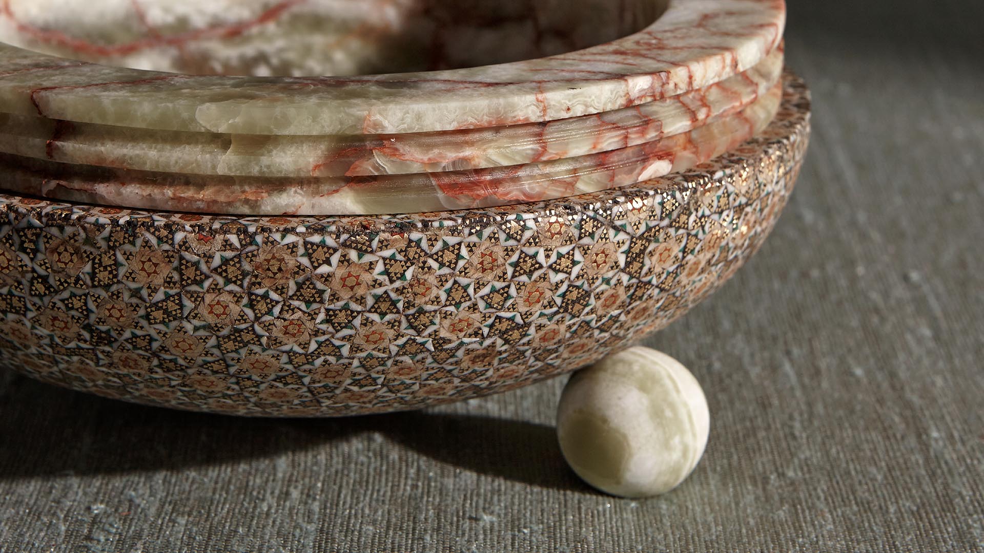 Close-up of a textured mosaic ceramic bowl with layered rim resting on a rough stone surface with a small marble sphere beneath it