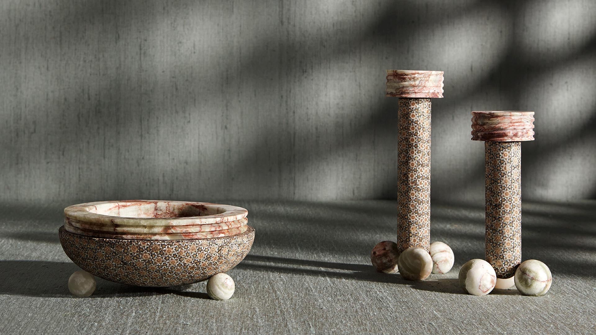 Textured stone bowl and two cylindrical columns with marble spheres on a gray stone surface under soft light shadows