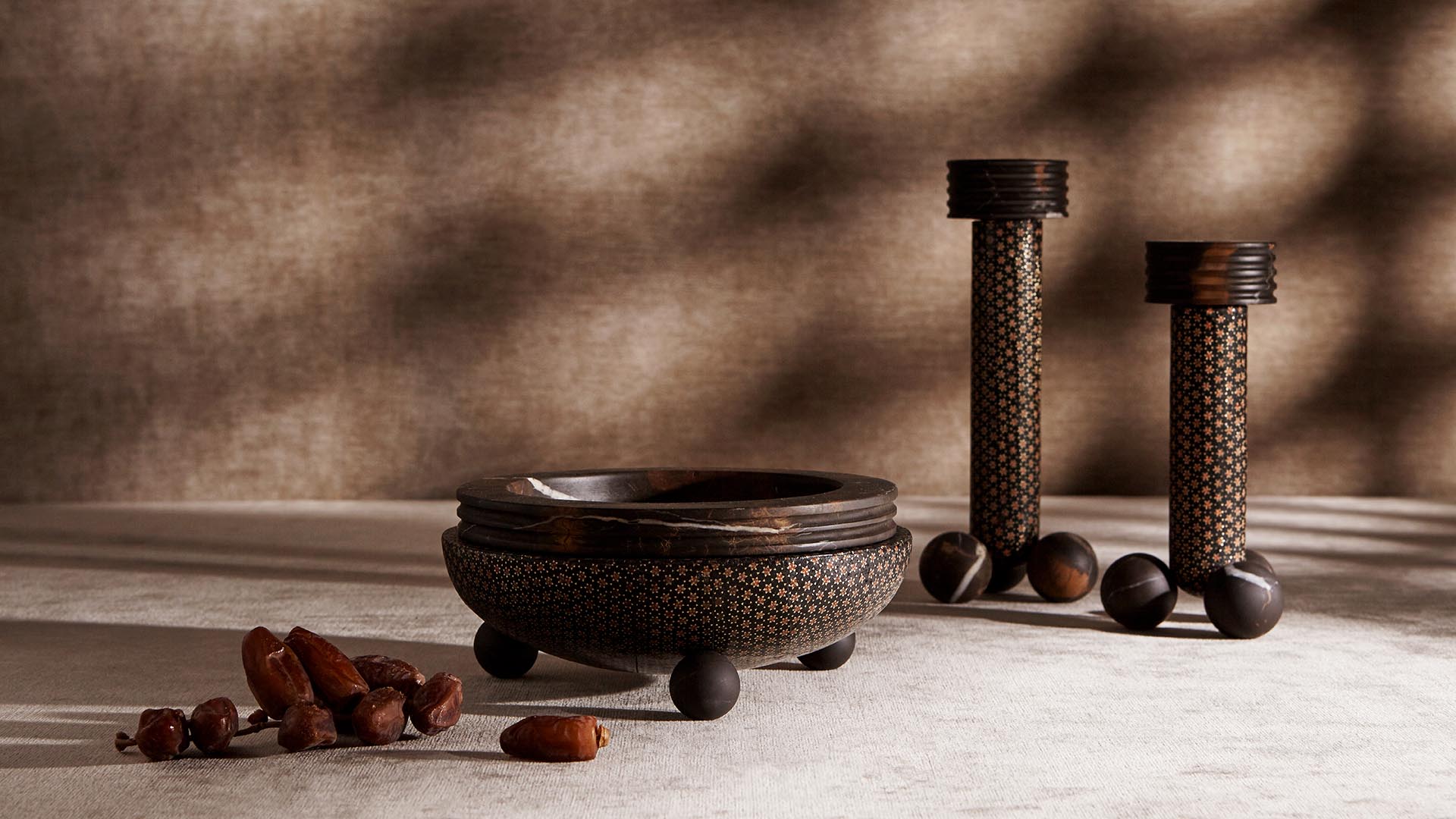 Low-angle view of three dark textured decorative objects with spherical bases and scattered acorns on a neutral surface and background