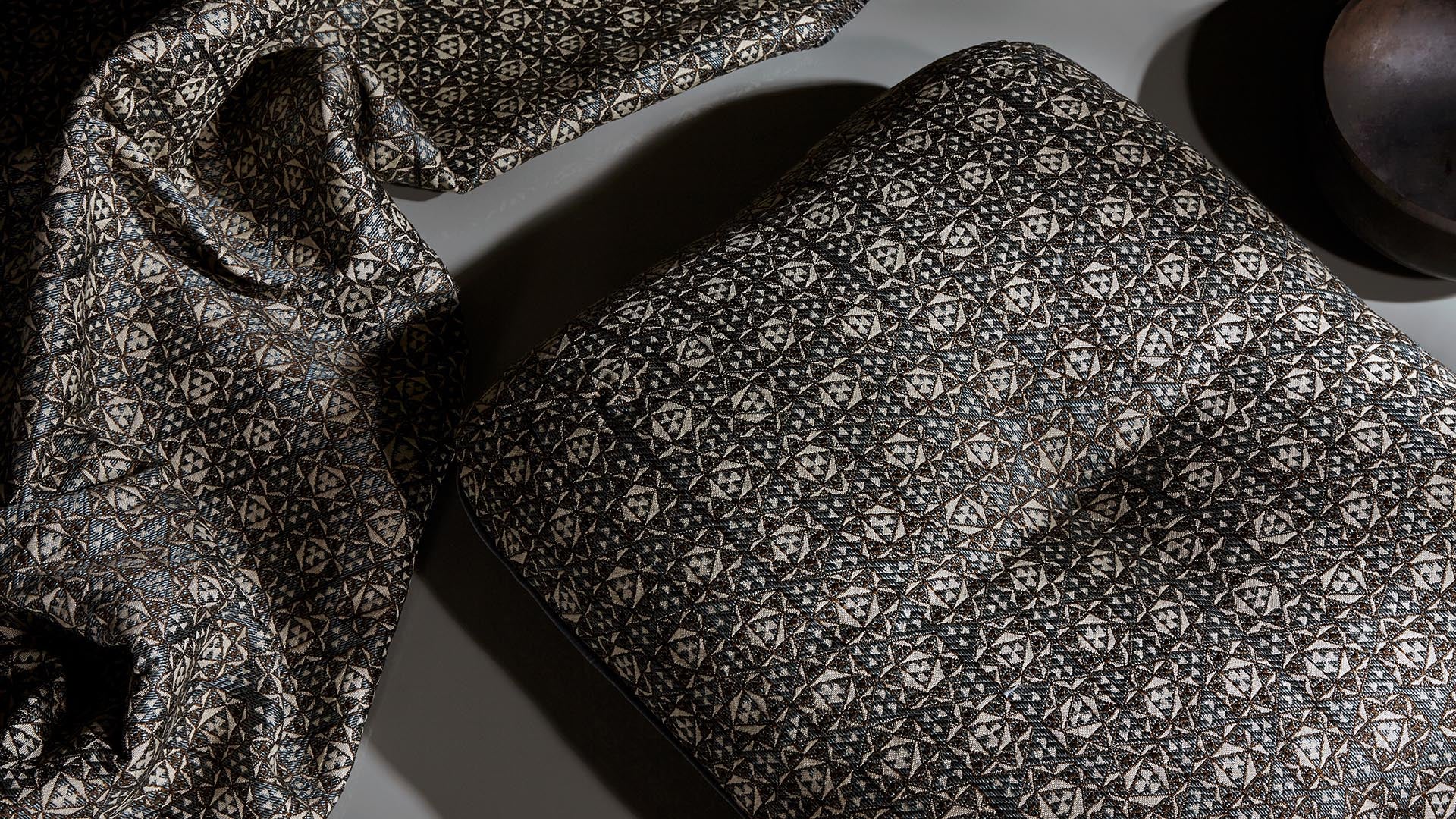 Close-up of a textured fabric with geometric patterns draped next to a matching patterned cushion on a neutral surface