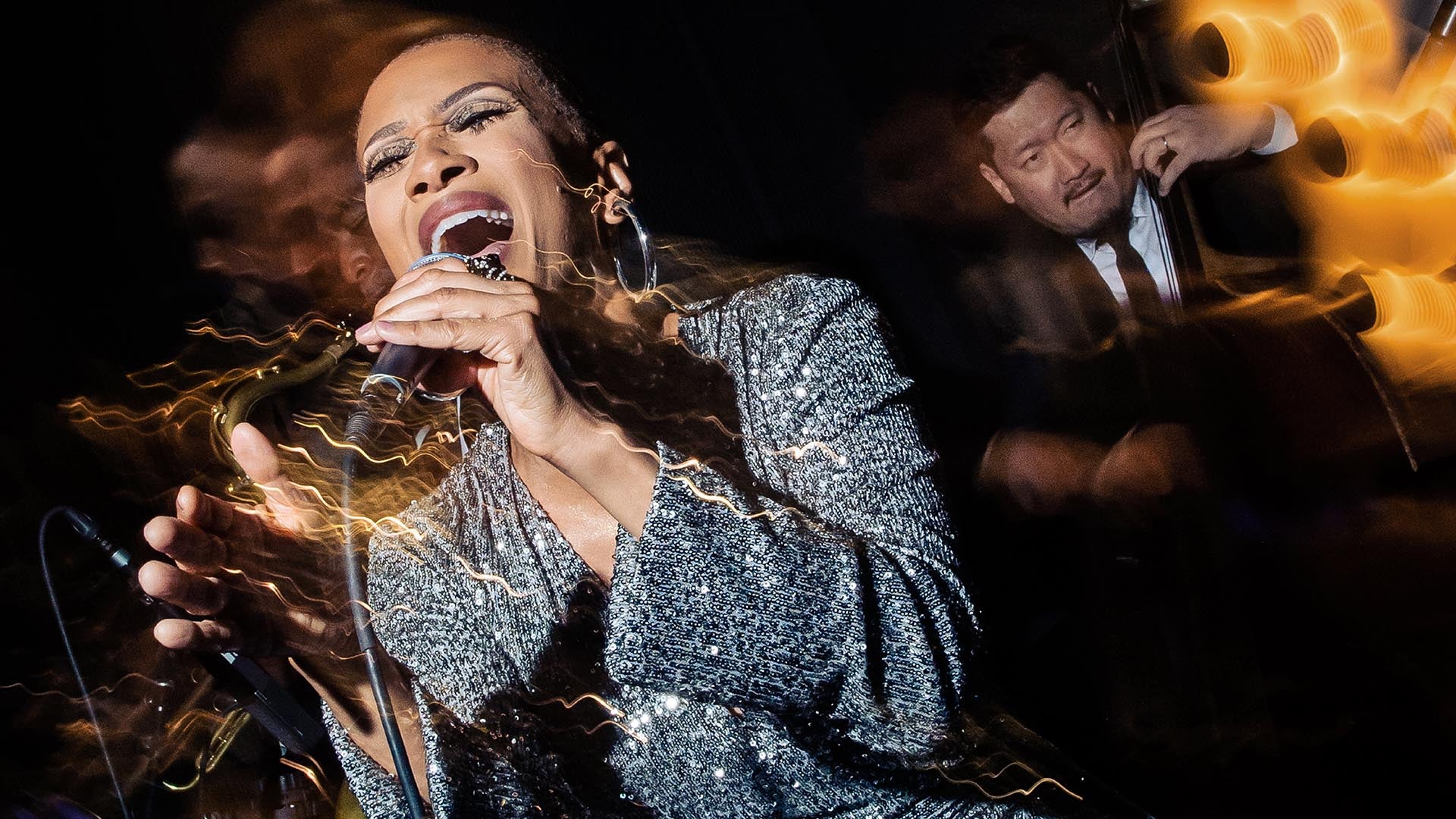 Close-up of a female singer passionately performing with blurred motion effects and a musician playing double bass in the background