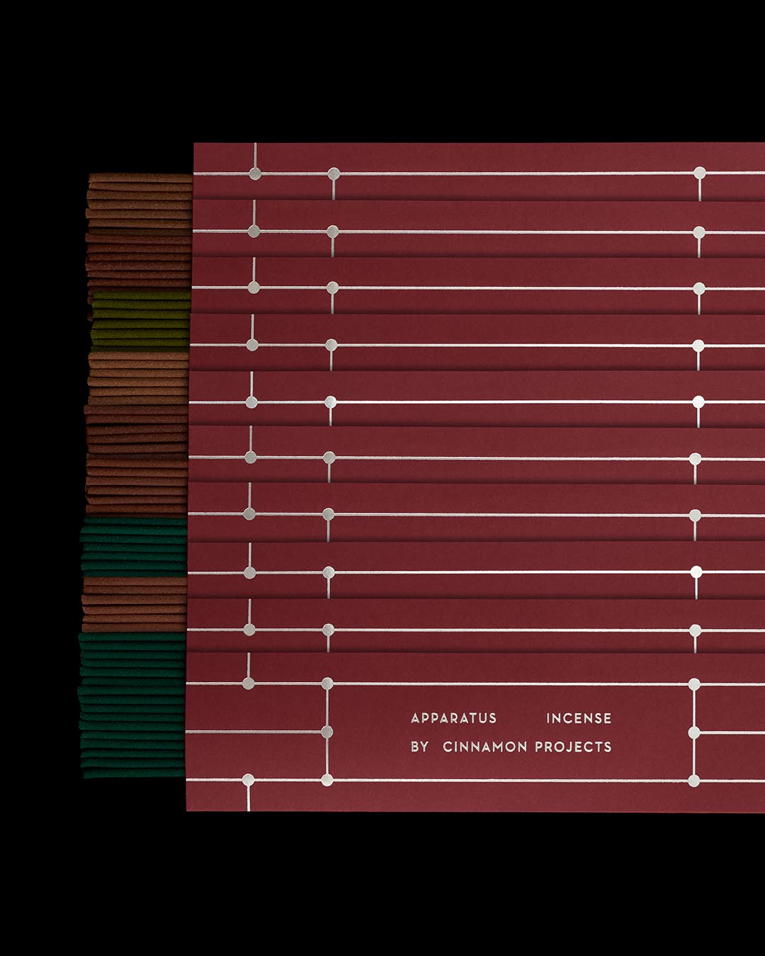 Stacked incense sticks in varied earth tones beside burgundy rectangular packaging with minimal white line design on a black background