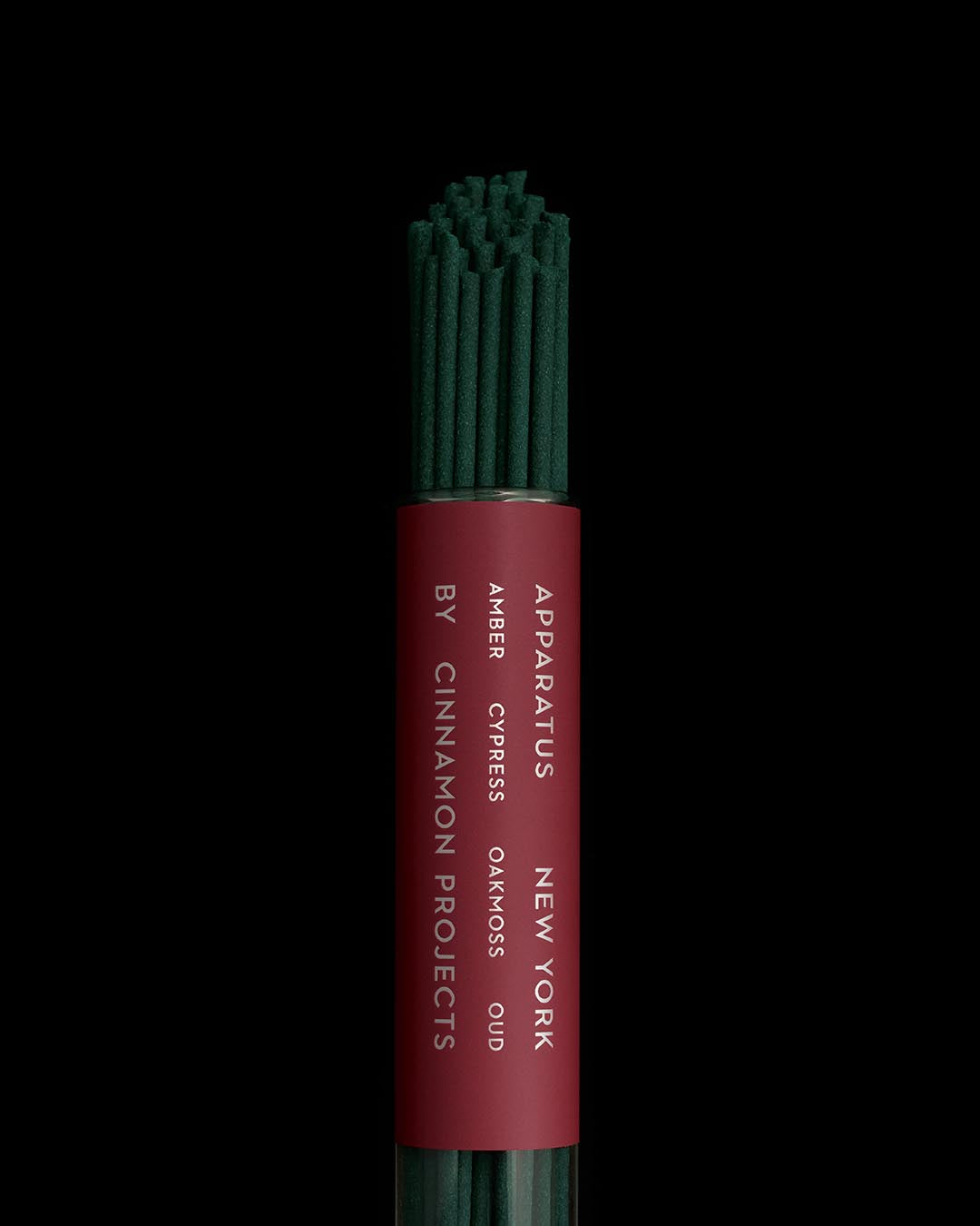 Close-up of green incense sticks bundled with a deep red label showing fragrance notes and brand name on black background