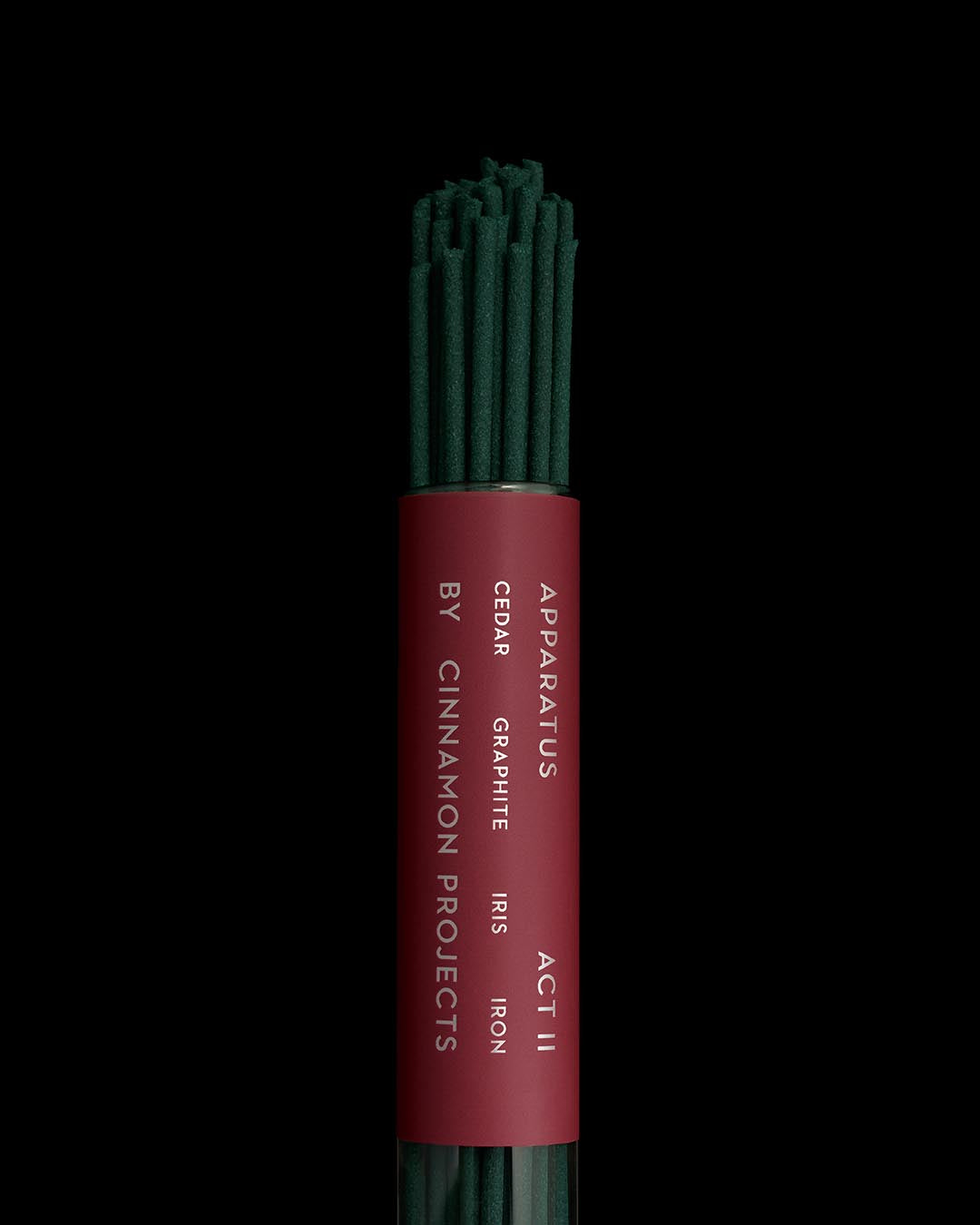 Bundle of dark green incense sticks in a cylindrical transparent container with a red label displaying product details on black background