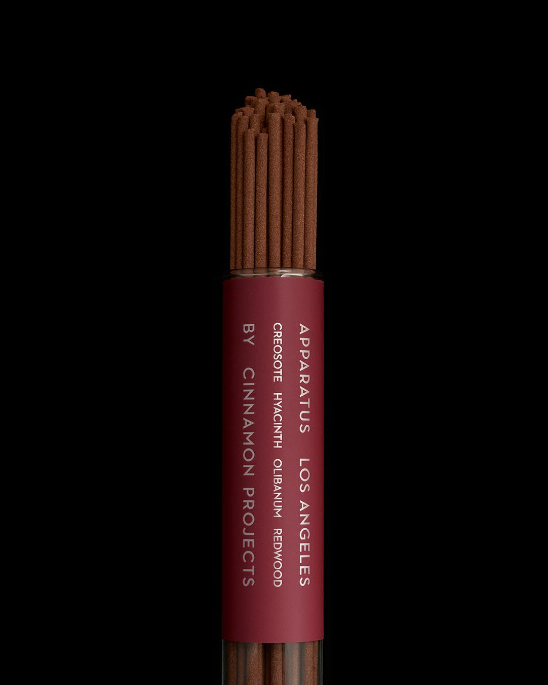 Close-up of a bundle of brown incense sticks labeled Apparatus Los Angeles by Cinnamon Projects against a black background