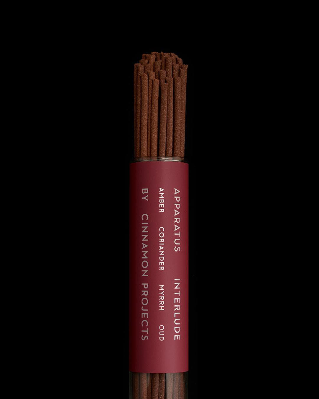 Close-up of brown incense sticks bundled in a maroon cylindrical holder with white text on a black background