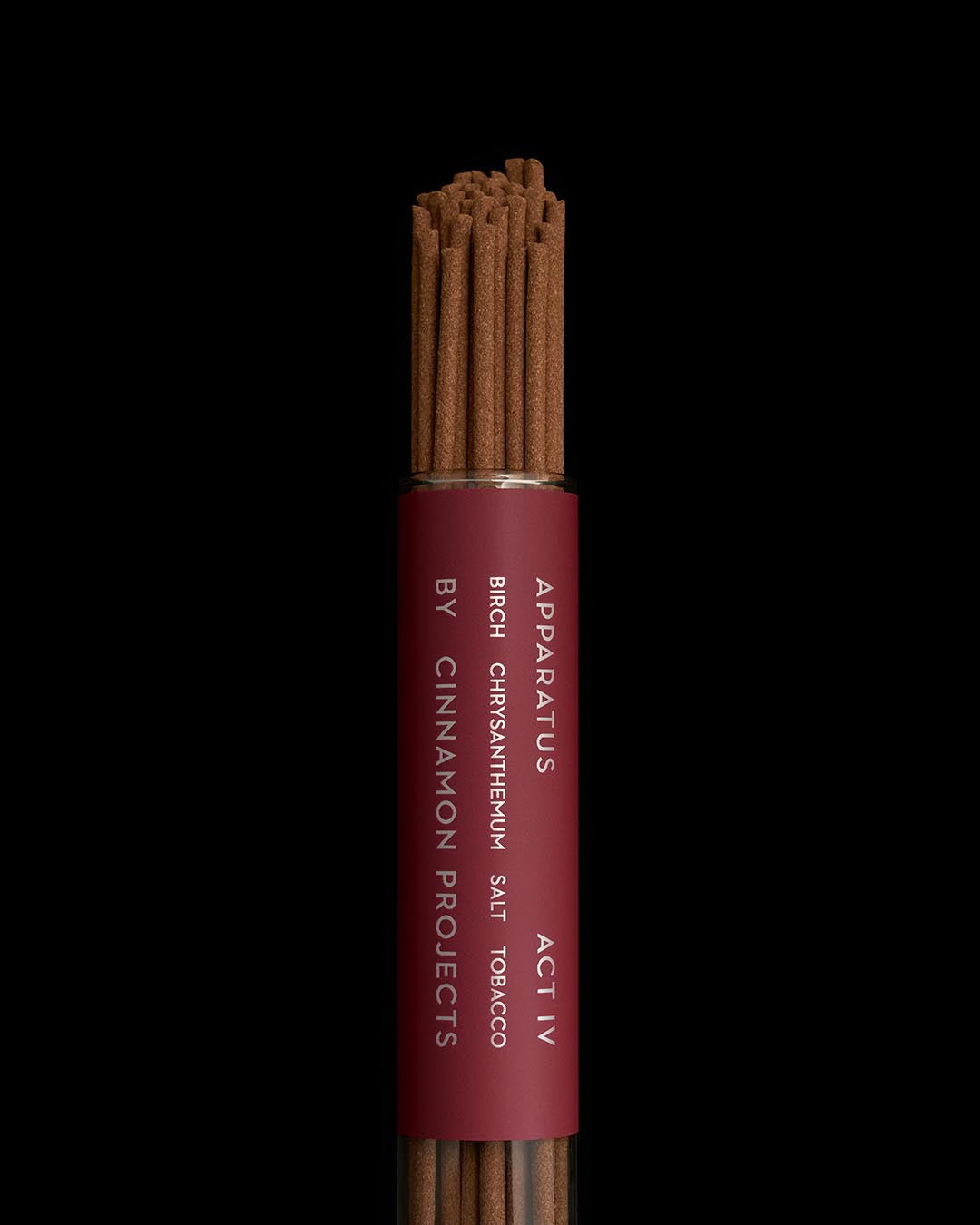 Close-up of brown incense sticks bundled in a maroon cylindrical container with white text on black background