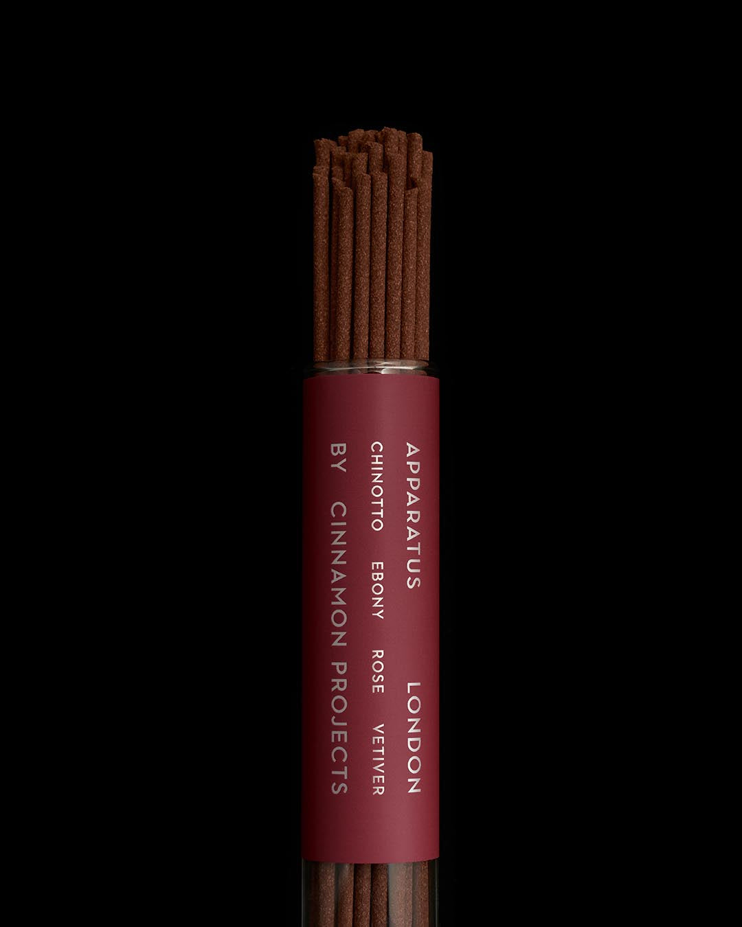 Close-up of dark brown incense sticks in a transparent tube with maroon label displaying product details on black background