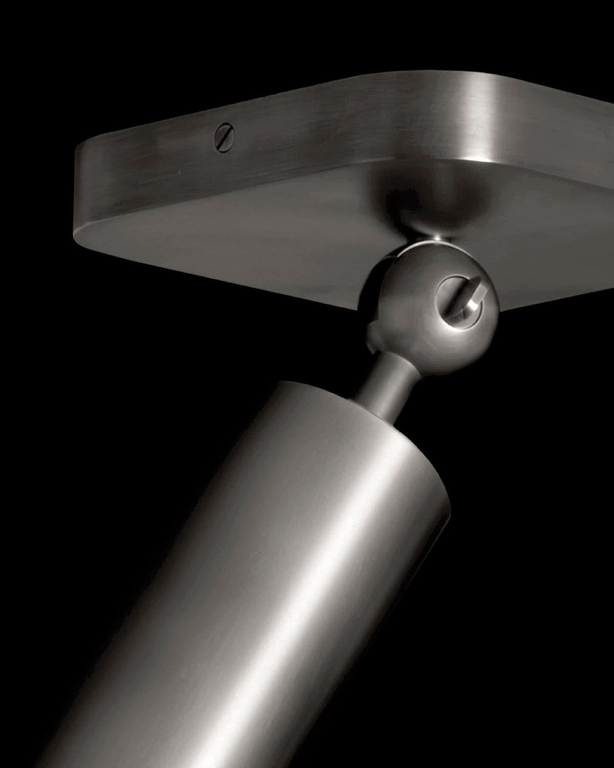 Close-up of a brushed metal cylinder downlight fixture with adjustable joint against a black background