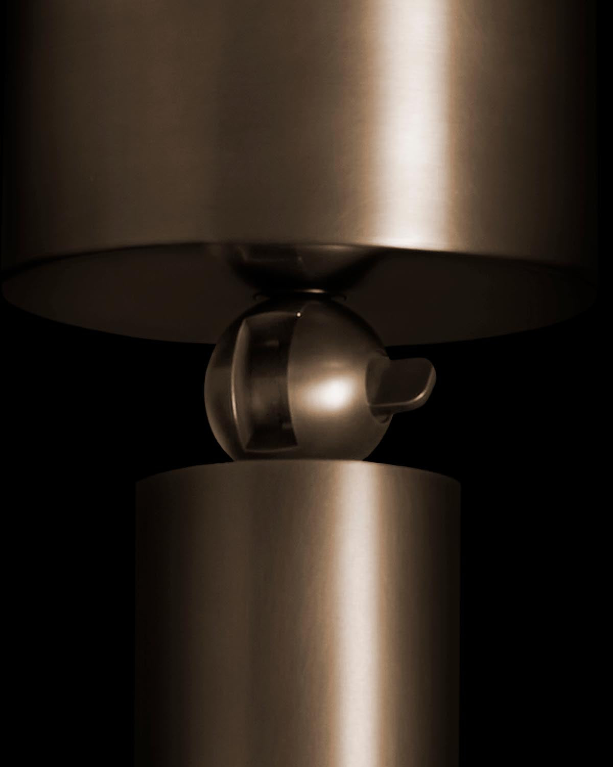 Close-up of a metallic round downlight fixture highlighting its smooth cylindrical body and spherical connector on a black background