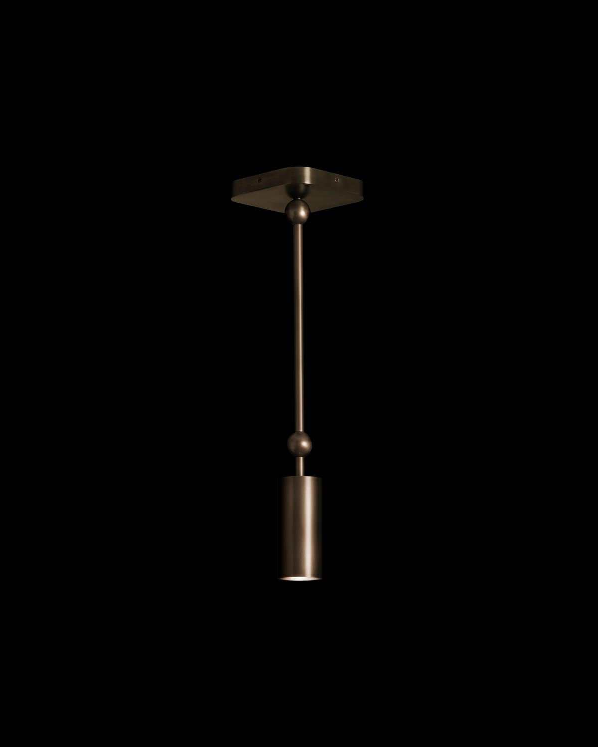 Minimalist metallic cylinder downlight pendant with extended rod and spherical accents against a black background
