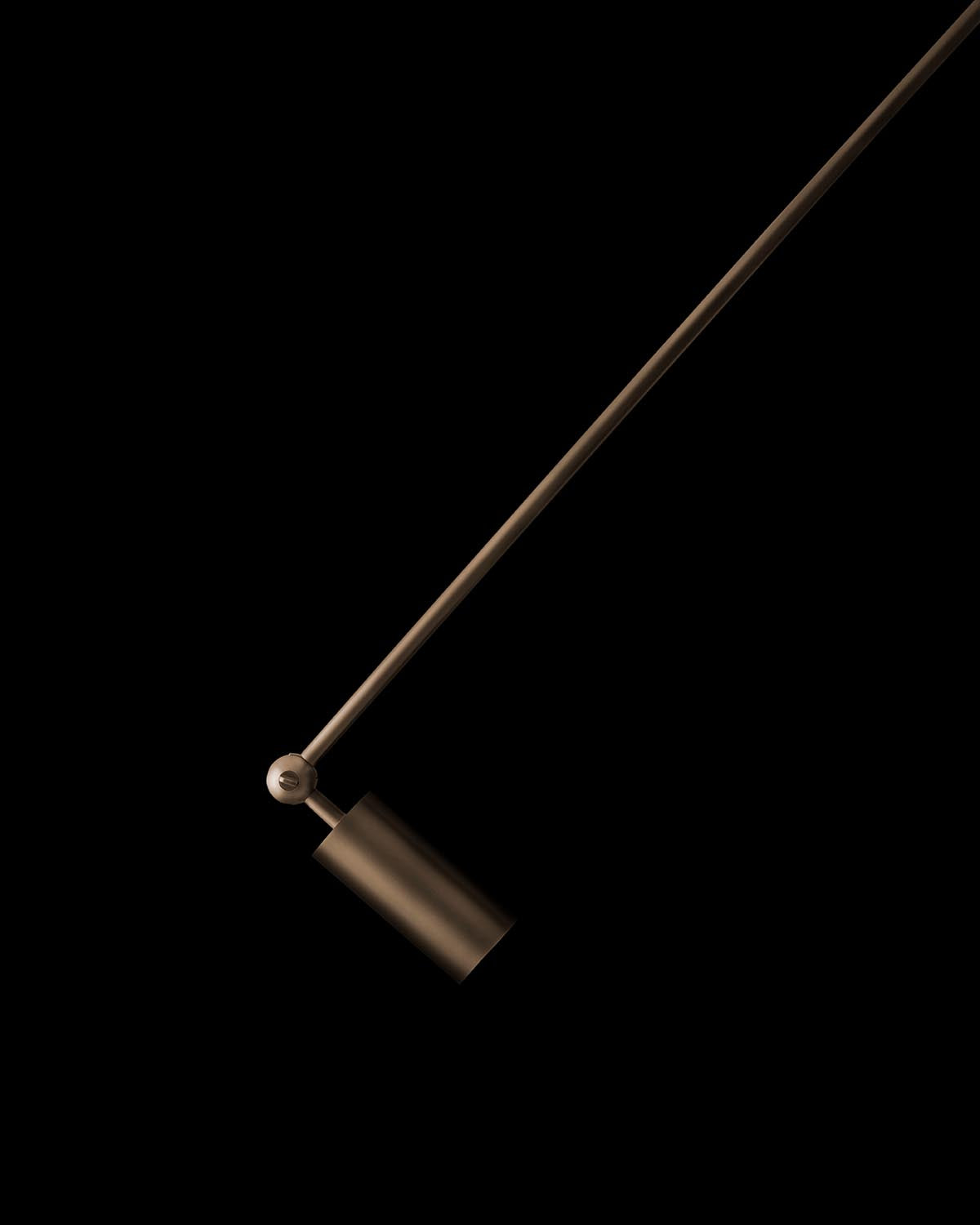 Close-up of a slim dark bronze extended downlight fixture with cylindrical head and angled arm against black background