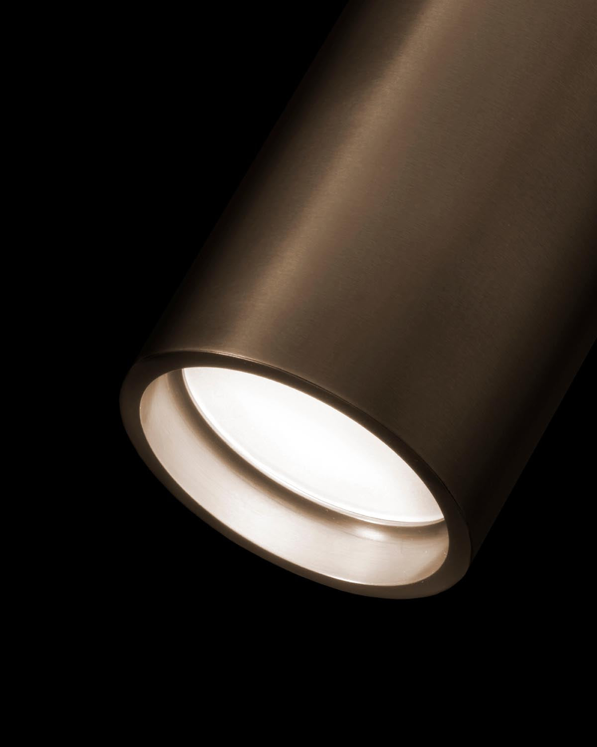 Close-up of a cylindrical downlight fixture with a bronze finish and bright white light against a black background