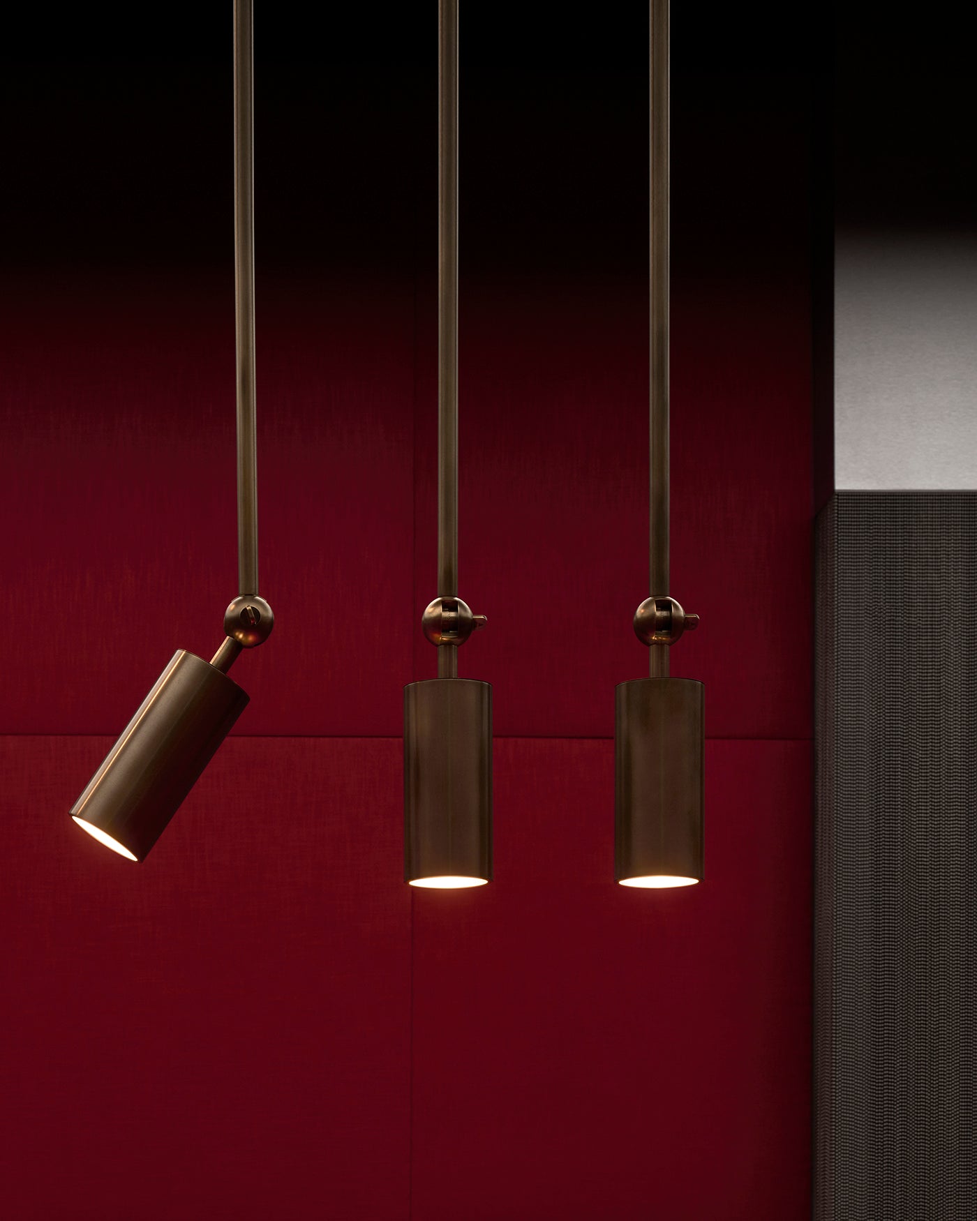 Three dark bronze cylindrical downlight pendants hanging against a deep red textured wall background