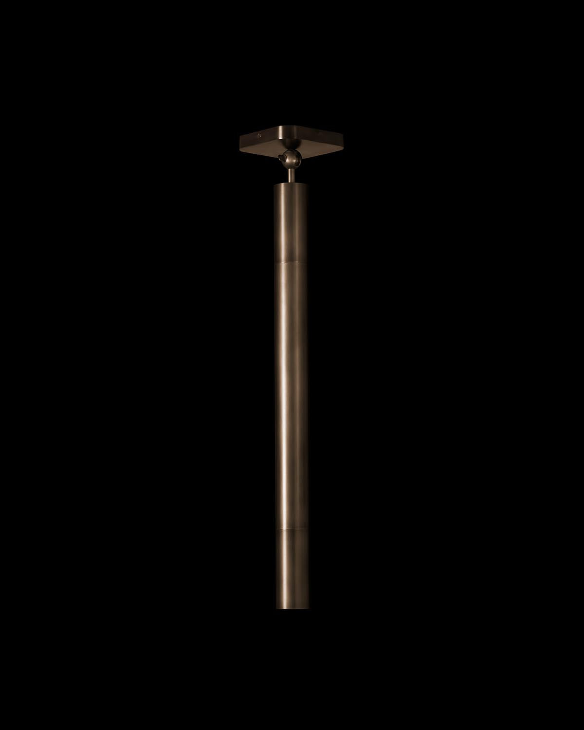 Close-up of a matte bronze cylindrical pendant light fixture with minimalist square ceiling mount on black background