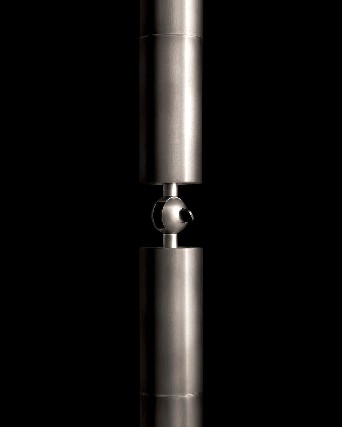 Close-up of a sleek cylindrical metal pendant light fixture with polished finish against a black background