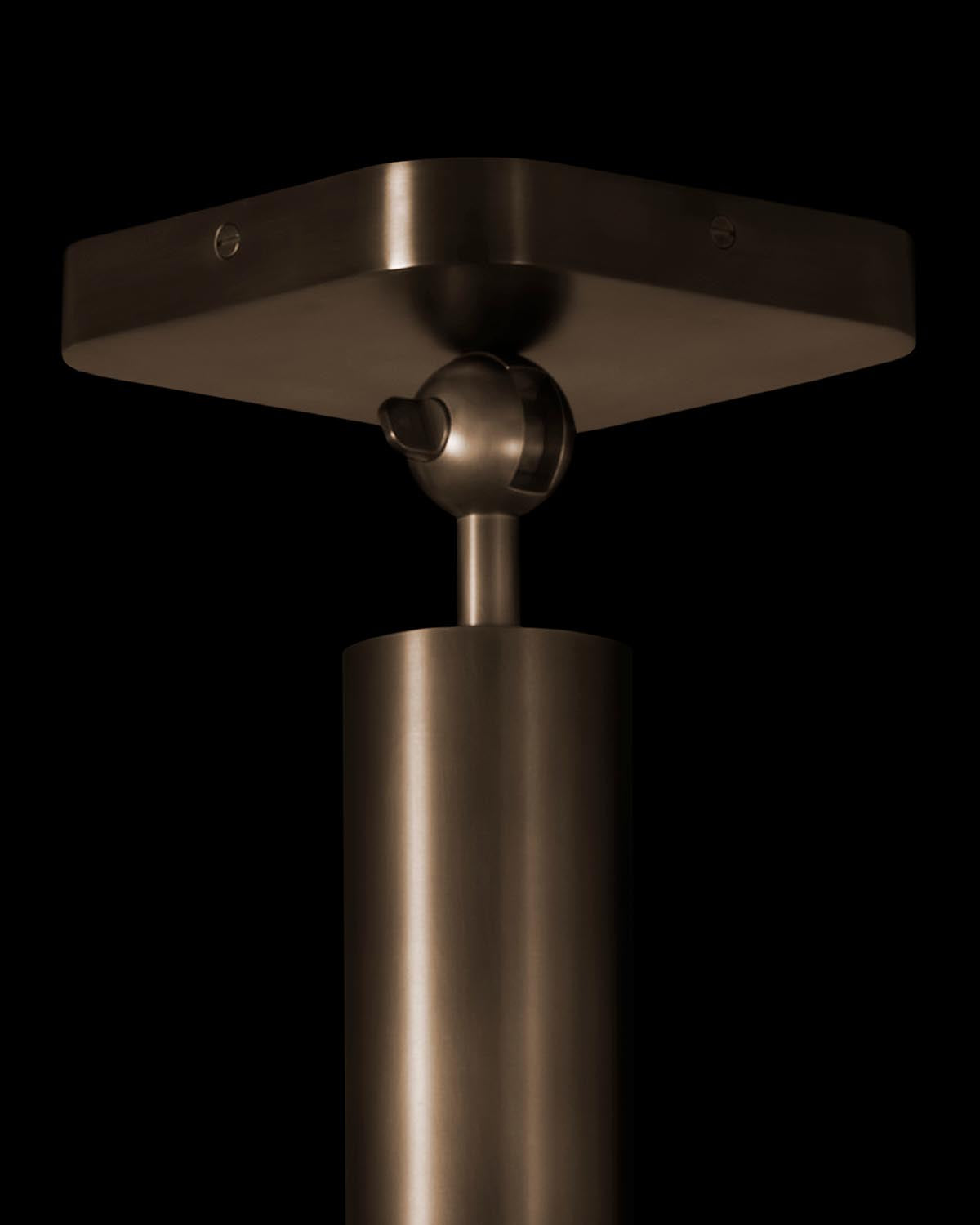 Close-up of cylindrical metal pendant light fixture with matte bronze finish against a black background