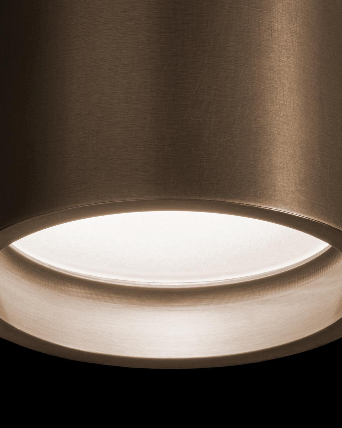 Close-up of cylindrical bronze pendant light with smooth metallic finish and diffused white glow inside against black background