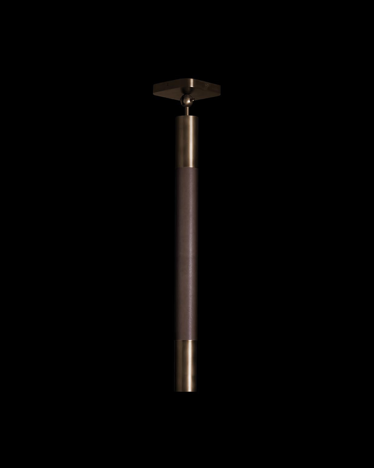 Close-up of a cylindrical pendant light with brass accents and dark textured body against a black background