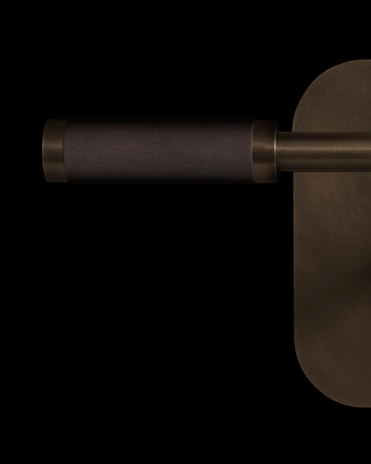 Close-up of a dark bronze reading sconce with cylindrical leather-wrapped arm and rounded backplate on black background