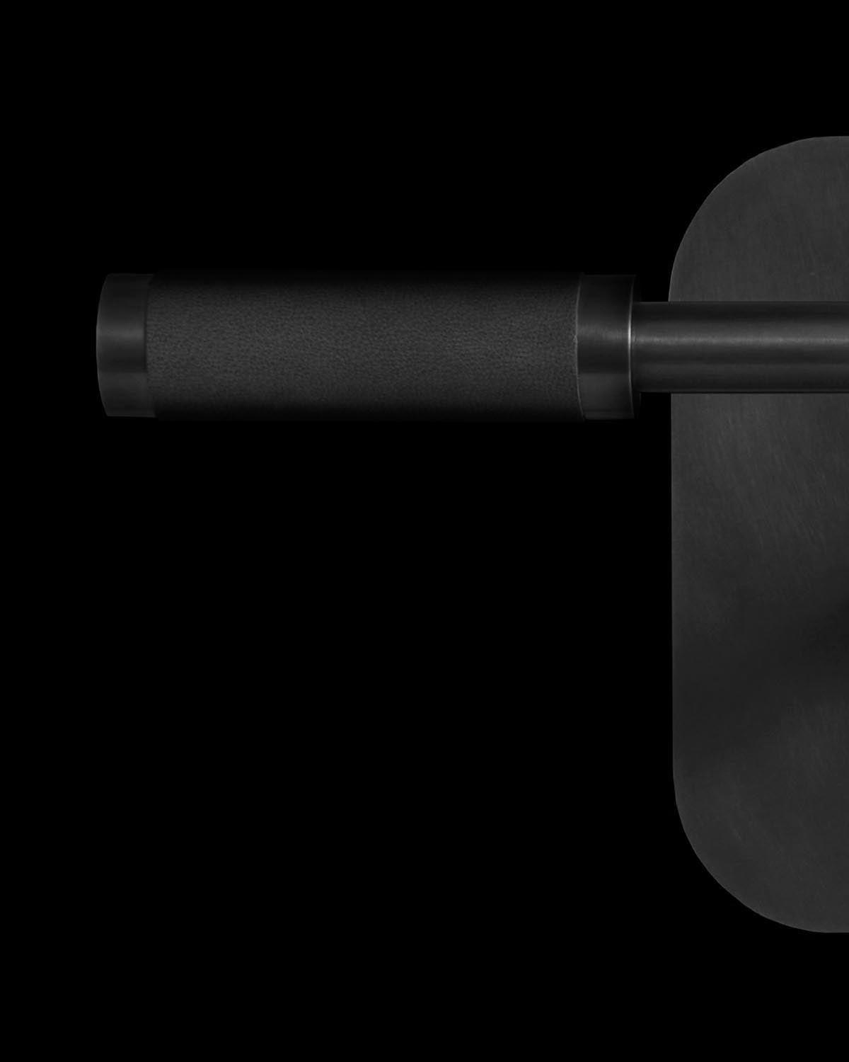 Close-up of black matte metal cylinder reading sconce arm with textured grip and oval wall mount on black background