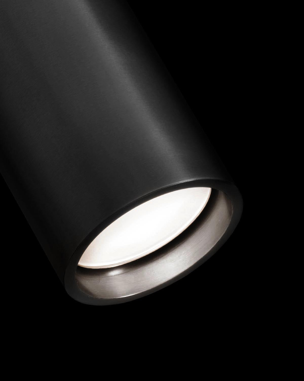 Close-up view of a black cylindrical reading sconce light fixture with a glowing bulb inside against a black background