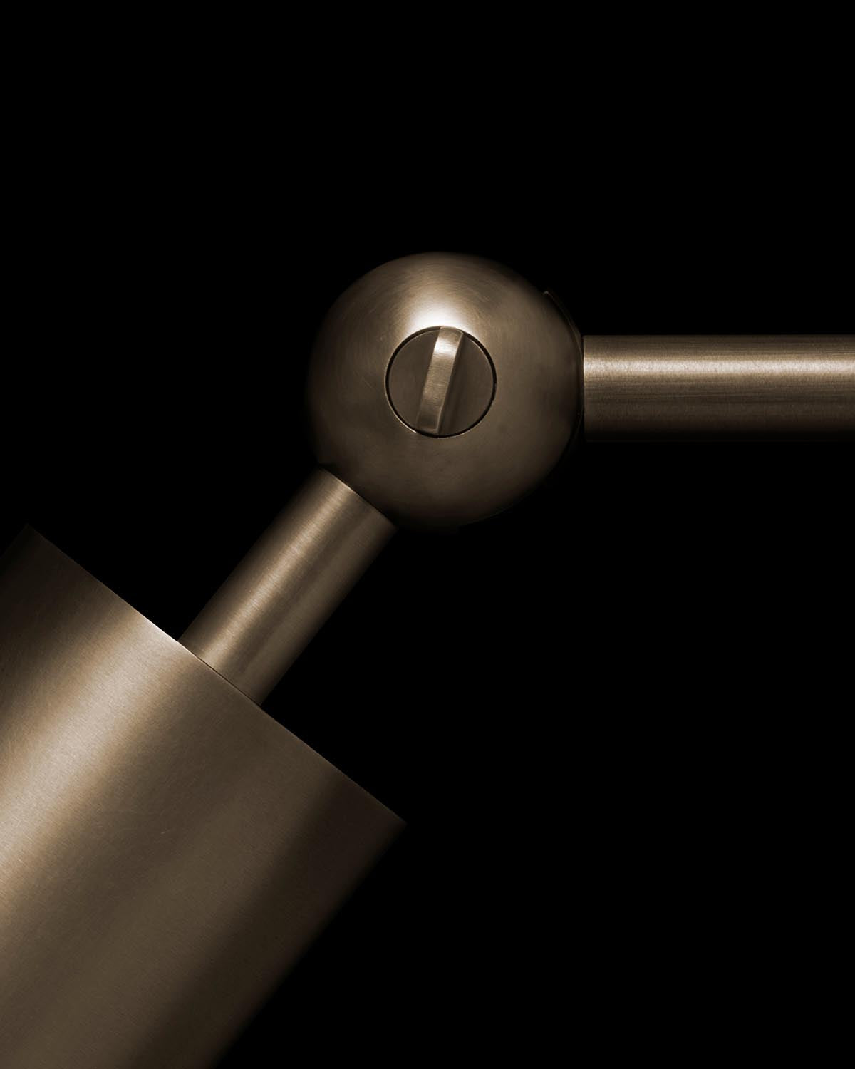 Close-up of bronze cylindrical wall sconce joint with visible screw and sleek metal finish on black background