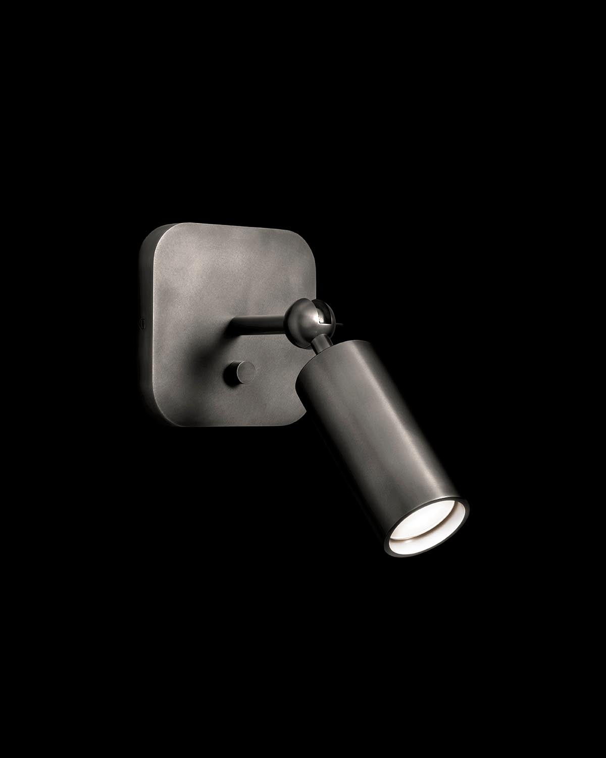 Minimalist black metal cylinder wall sconce with rounded square base and adjustable swivel spotlight on black background