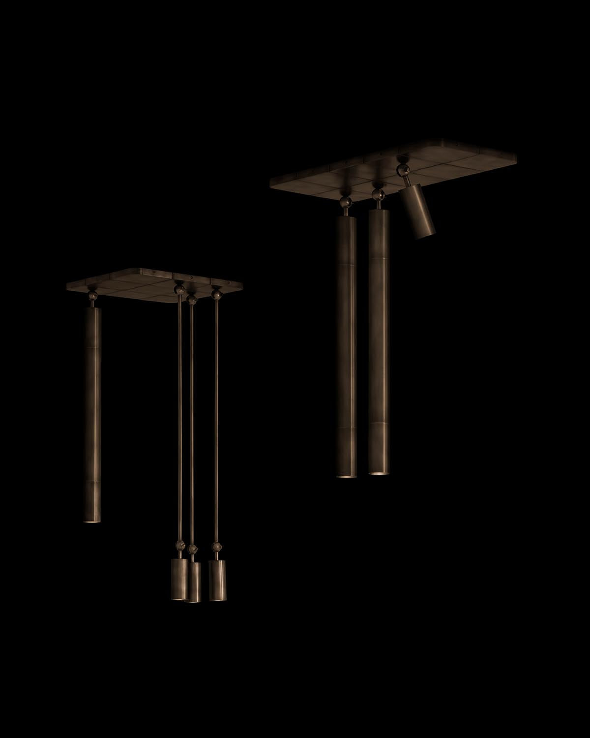 Two sets of cylindrical pendant lights with a metallic finish hanging from rectangular ceiling mounts on a black background