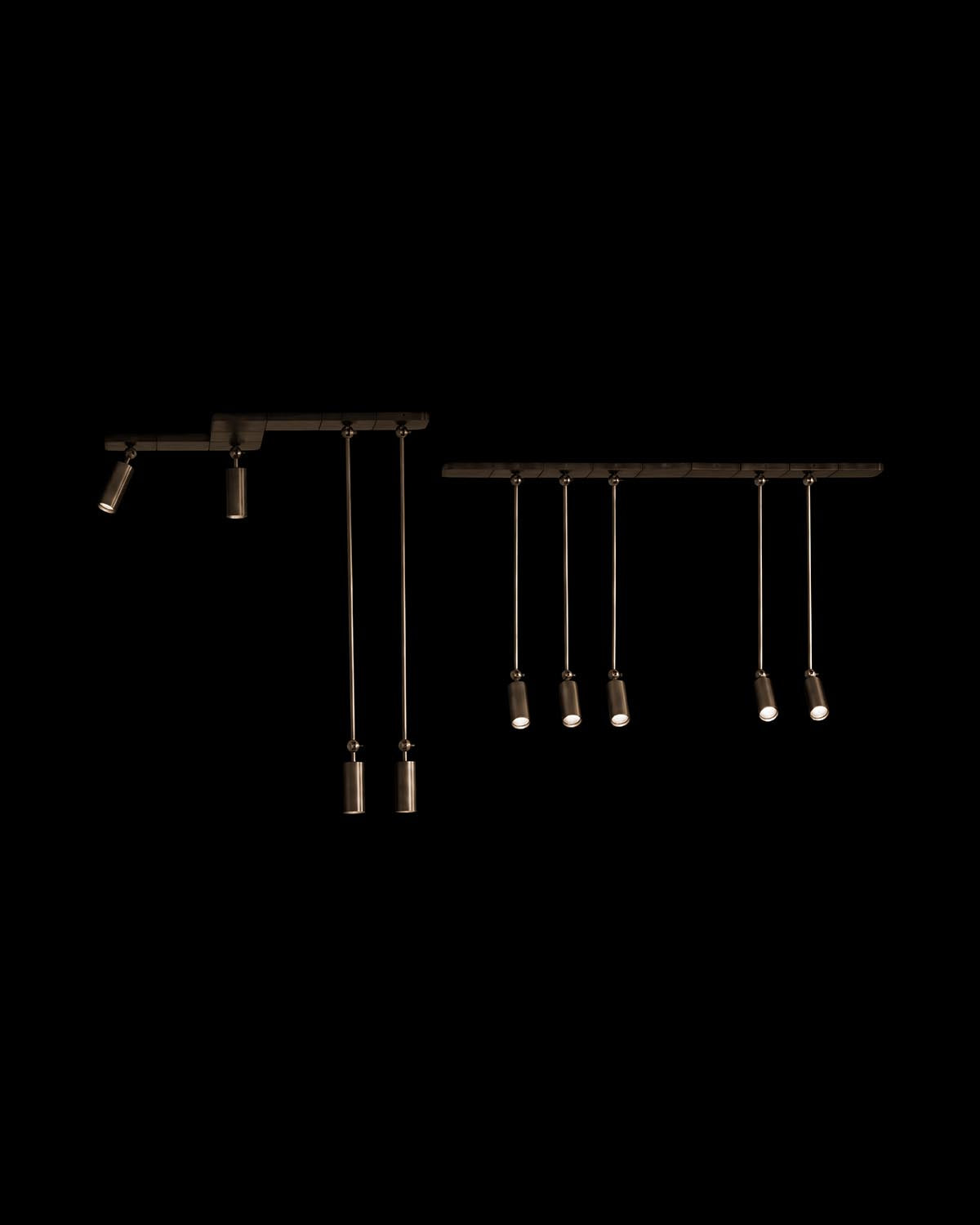 Two black metal pendant lighting systems with cylindrical fixtures hanging from horizontal bars against a black background