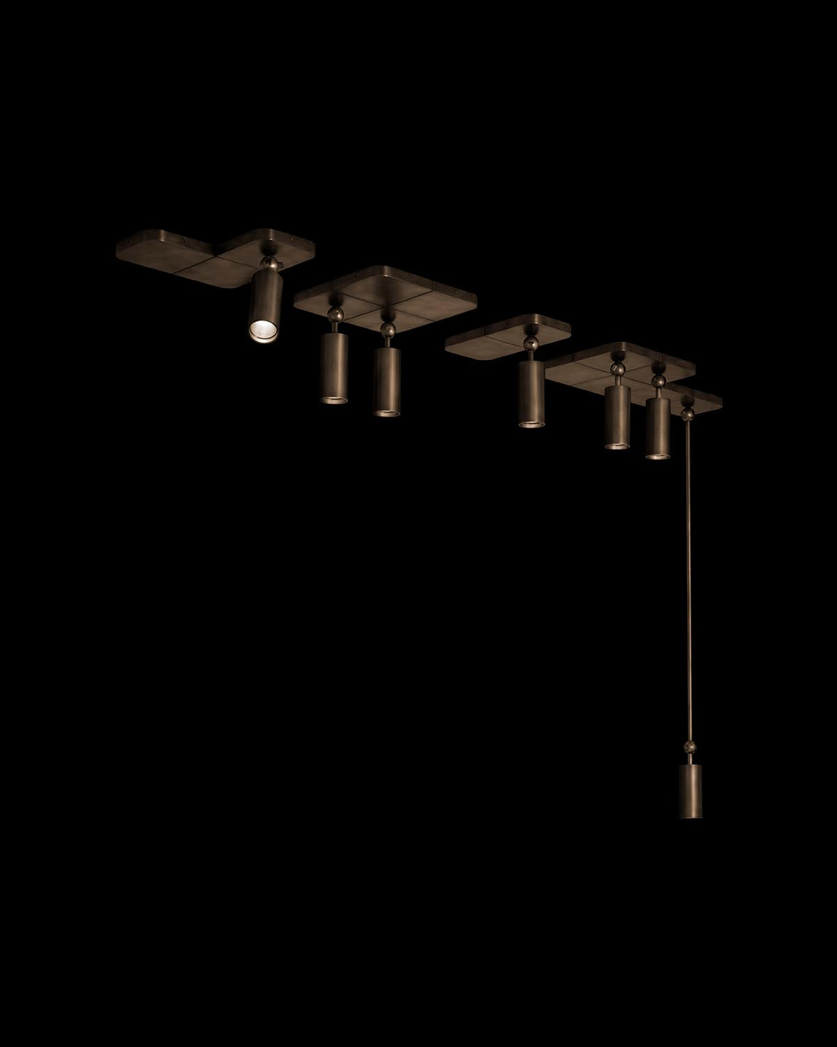 Linear arrangement of dark cylindrical pendant lights with varying lengths suspended from flat rectangular mounts on black background