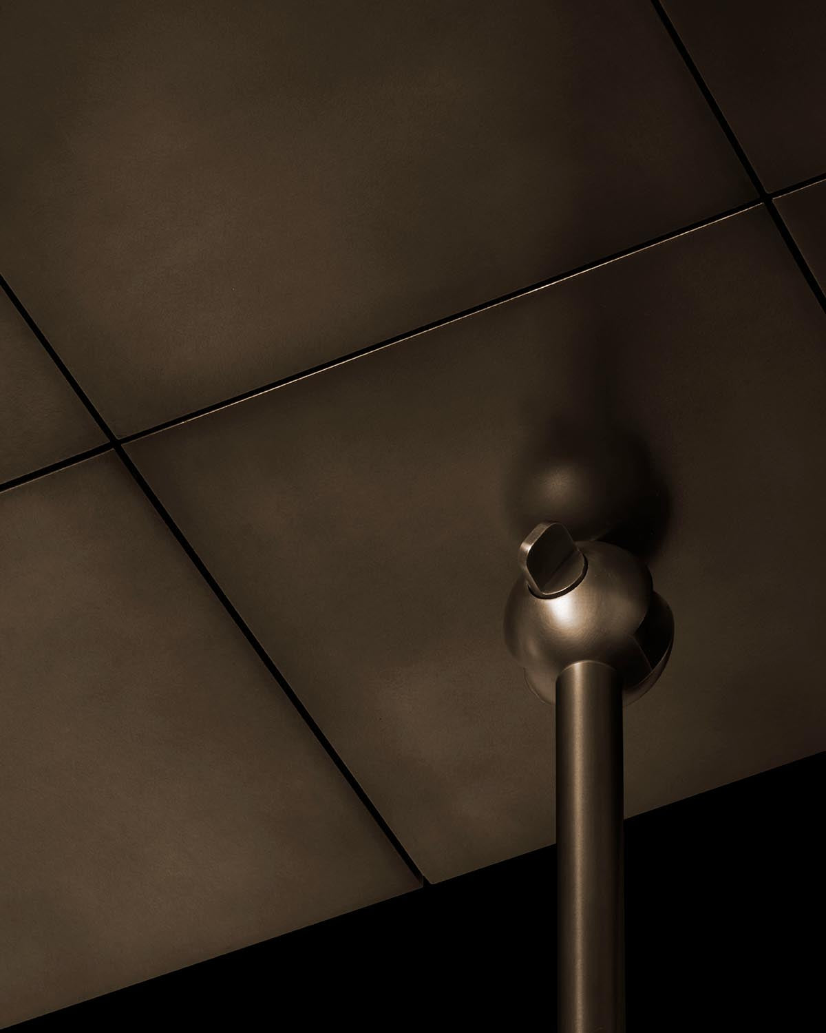 Close-up of a matte dark metallic cylindrical fixture attached to a square paneled ceiling with soft lighting and shadows