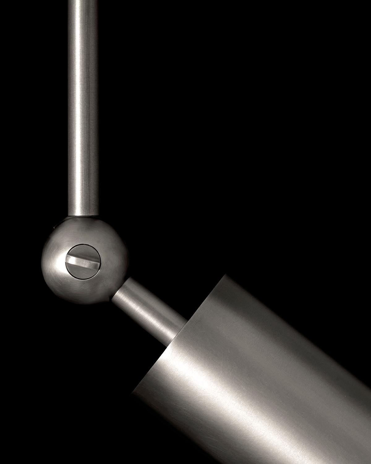 Close-up of a brushed metal cylindrical fixture joint with a spherical connector against a black background