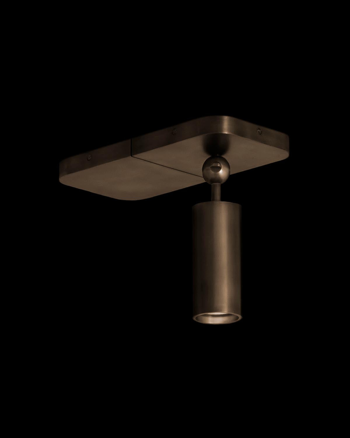 Ceiling-mounted cylindrical spotlight with a dark brushed metal finish against a black background