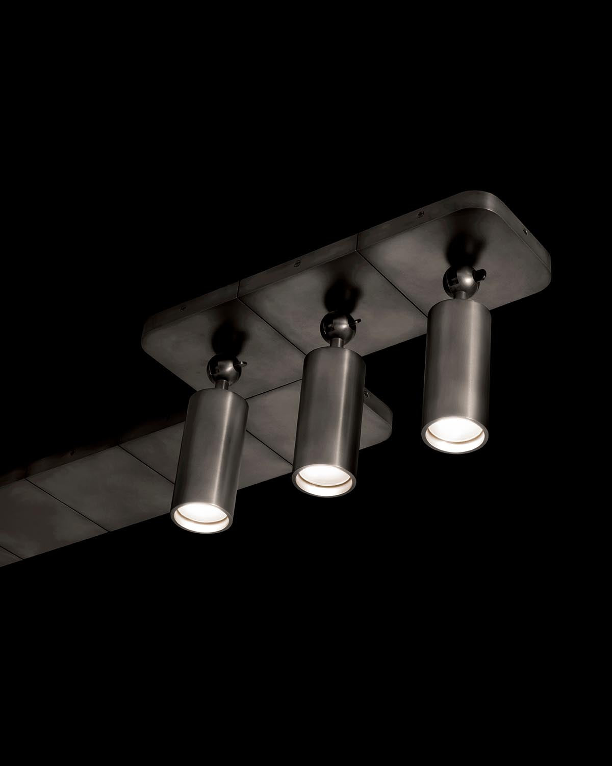 Close-up of three cylindrical black metal pendant lights attached to a rectangular ceiling mount against a black background