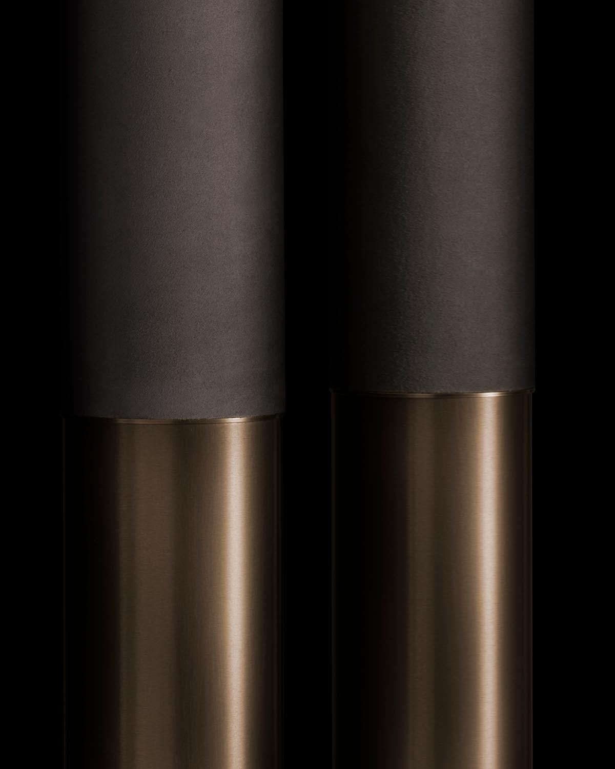 Close-up of two cylindrical objects with matte black upper parts and smooth metallic lower sections on a black background