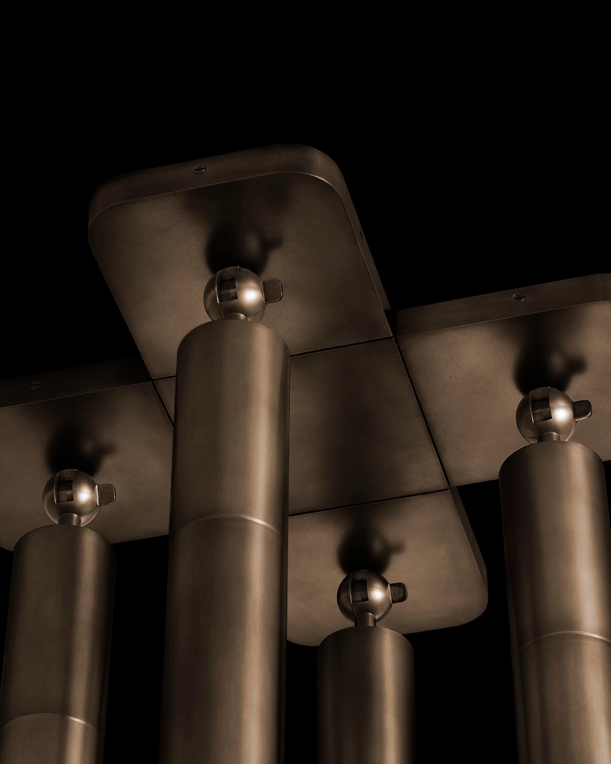 Close-up view of tall cylindrical metal columns with rounded tops and rectangular plates above on a black background