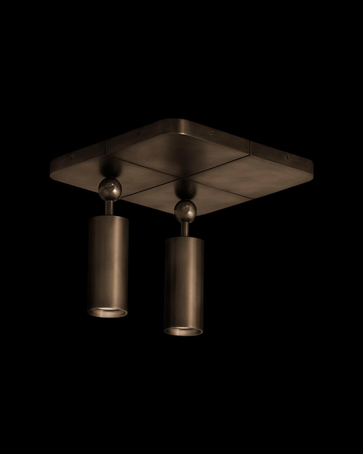 Square ceiling mount with two dark bronze cylindrical spotlights suspended from rounded pivots against black background