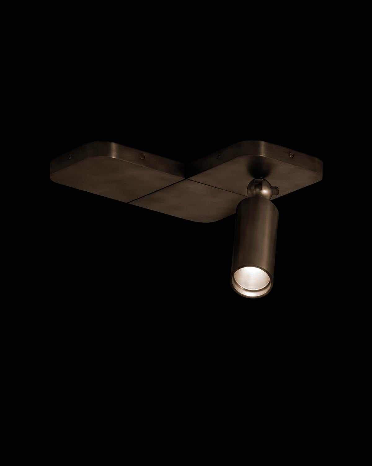 Single adjustable dark bronze spotlight mounted on a rectangular ceiling plate against black background