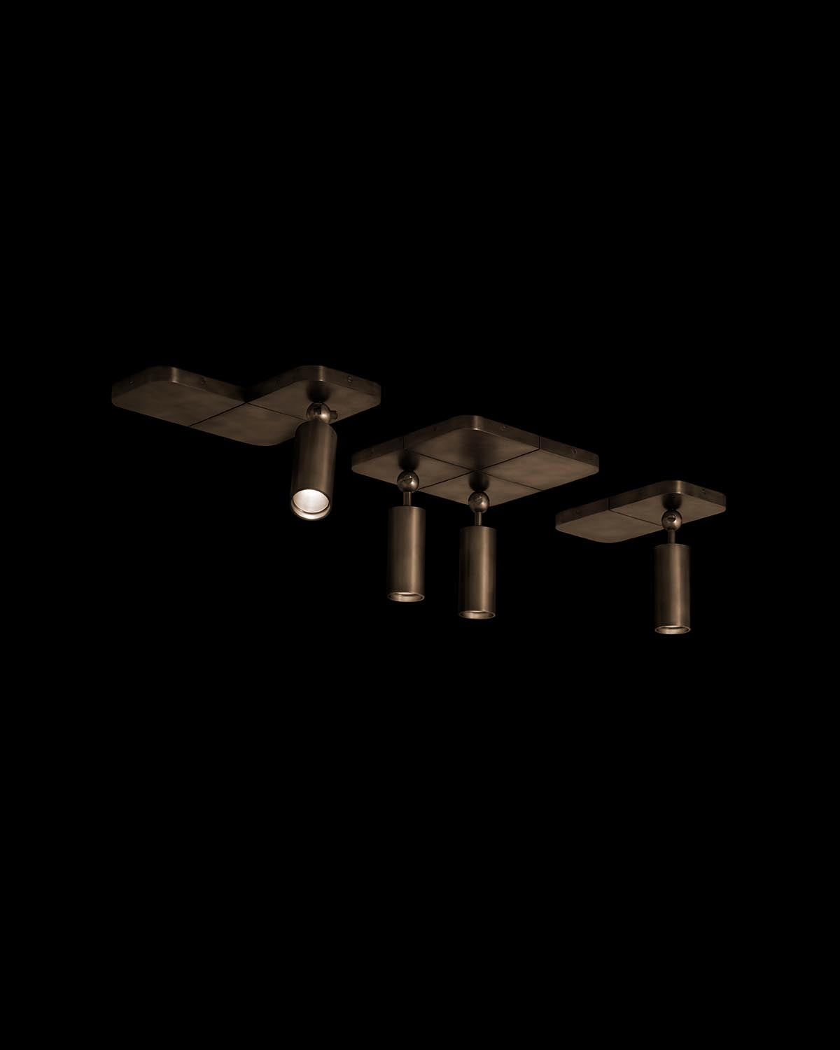 Four ceiling-mounted cylindrical spotlights with a dark bronze finish arranged in a linear pattern against black background