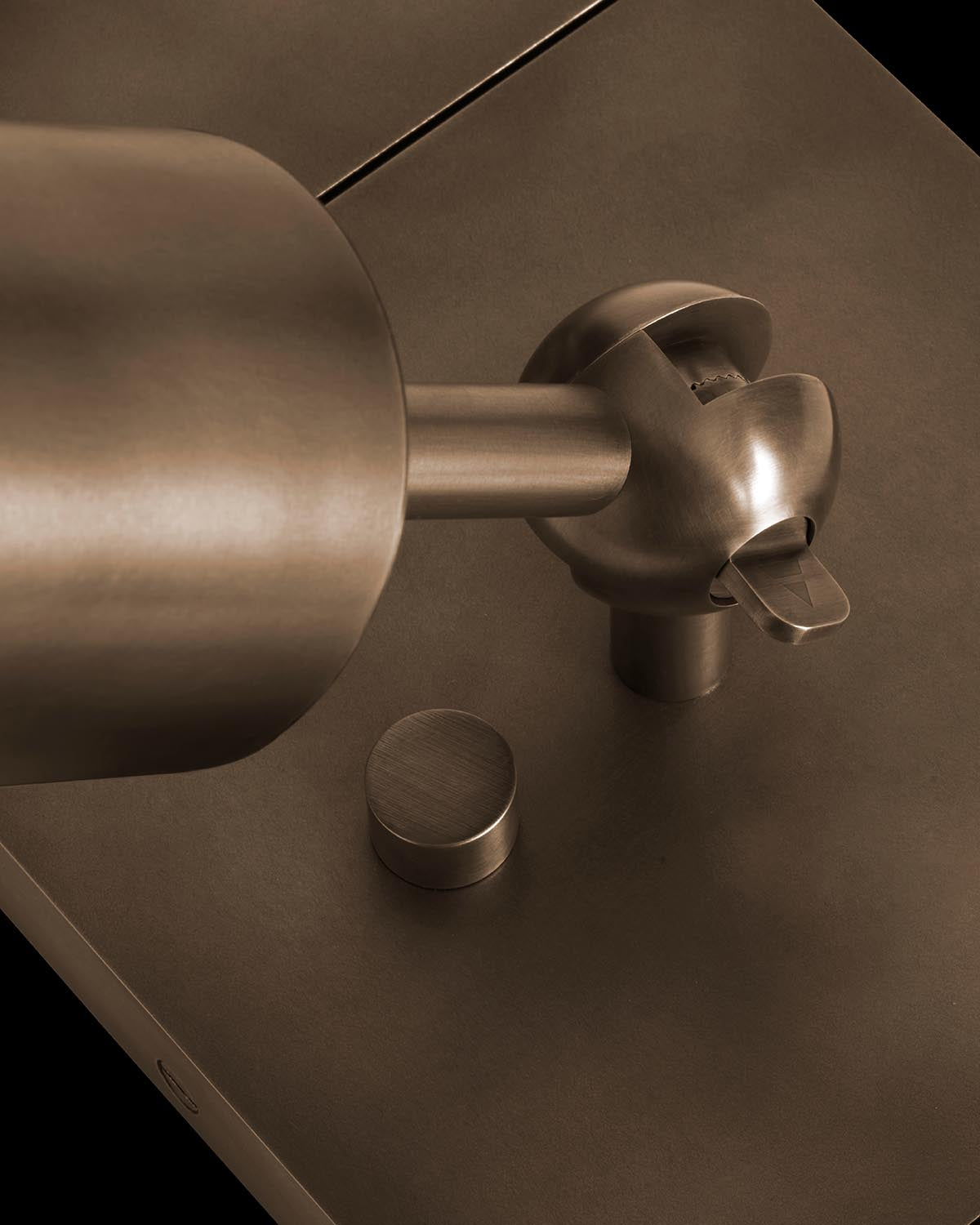 Close-up of a bronze cylindrical uplight fixture with a round base and adjustable swivel head on a dark background