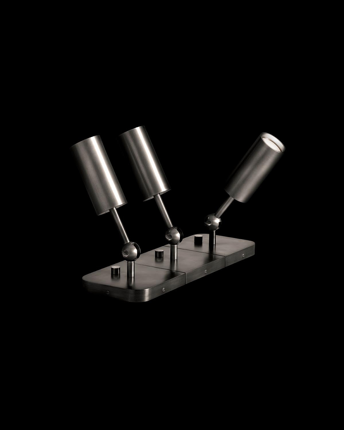 Three adjustable cylindrical uplights mounted on a rectangular metal base with matte black finish on black background