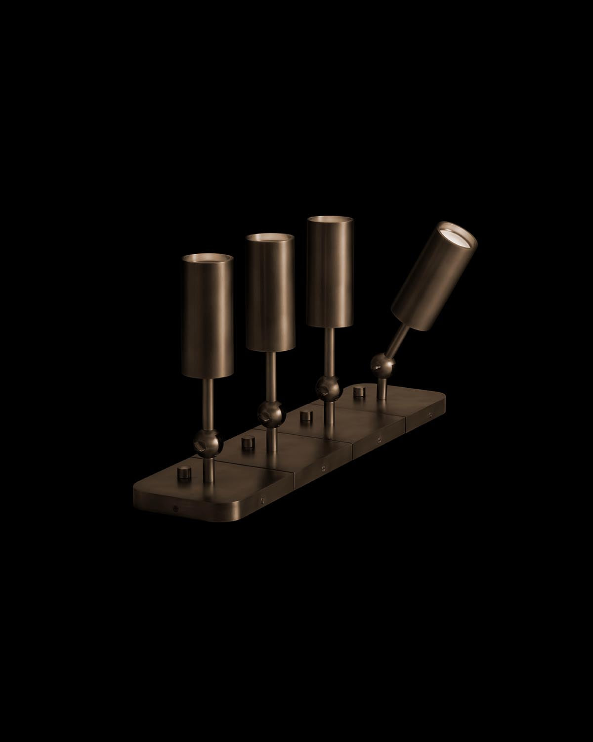 Row of four cylindrical uplight lamps in dark bronze finish mounted on rectangular base against black background