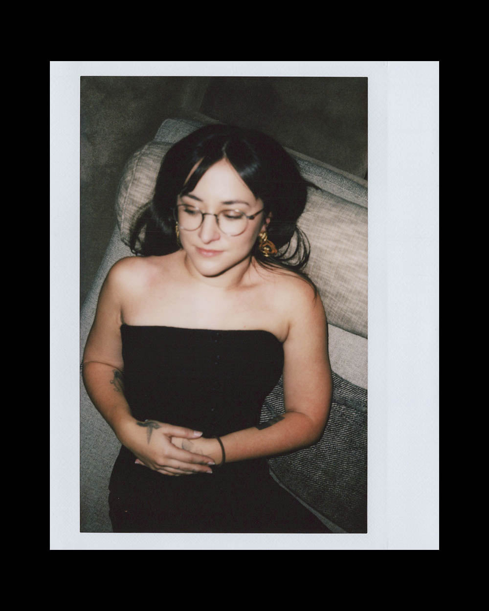 Young woman with glasses and dark hair reclining on a couch wearing a sleeveless black top with hands folded on her stomach