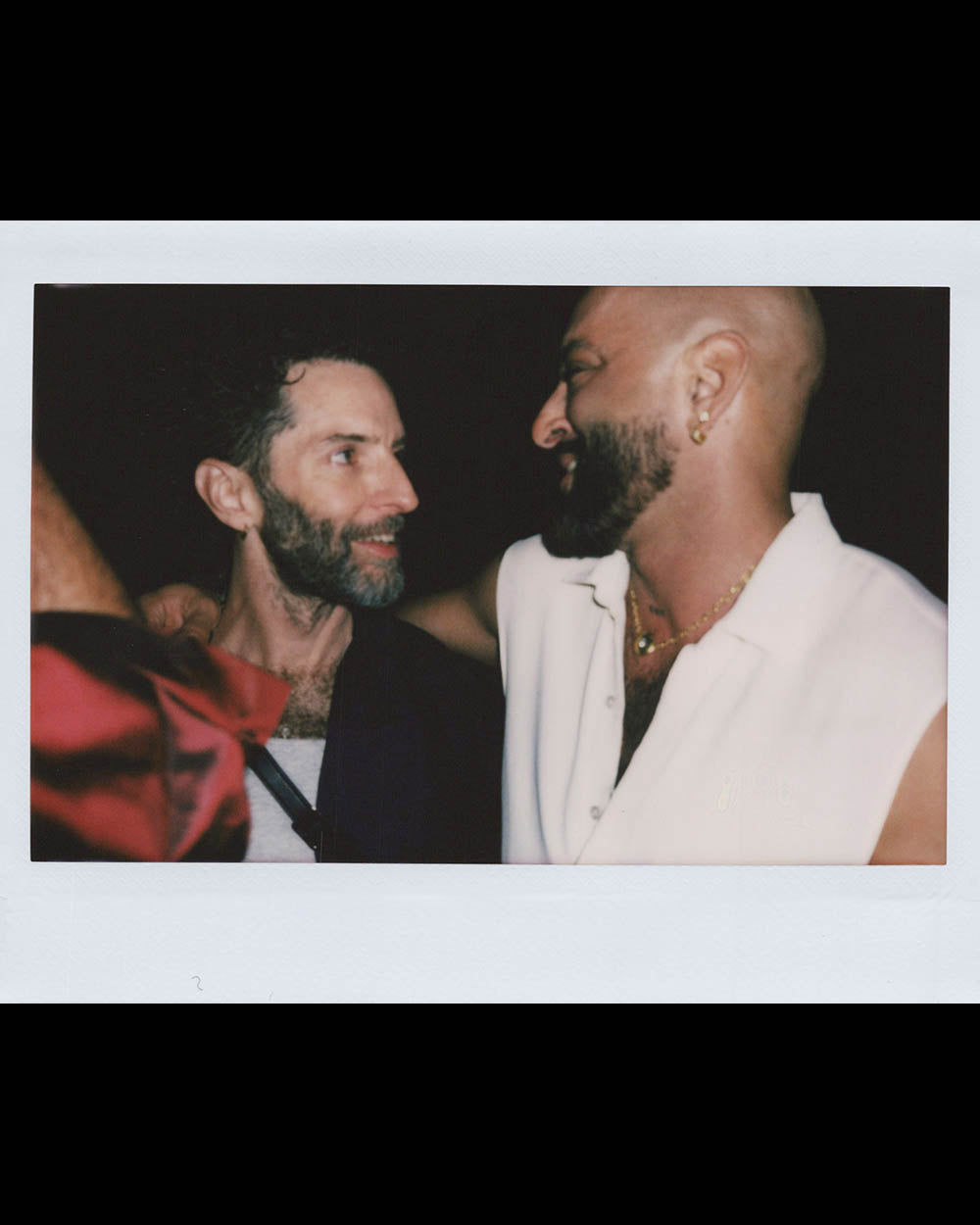 Two men smiling at each other in a close embrace against a dark background.